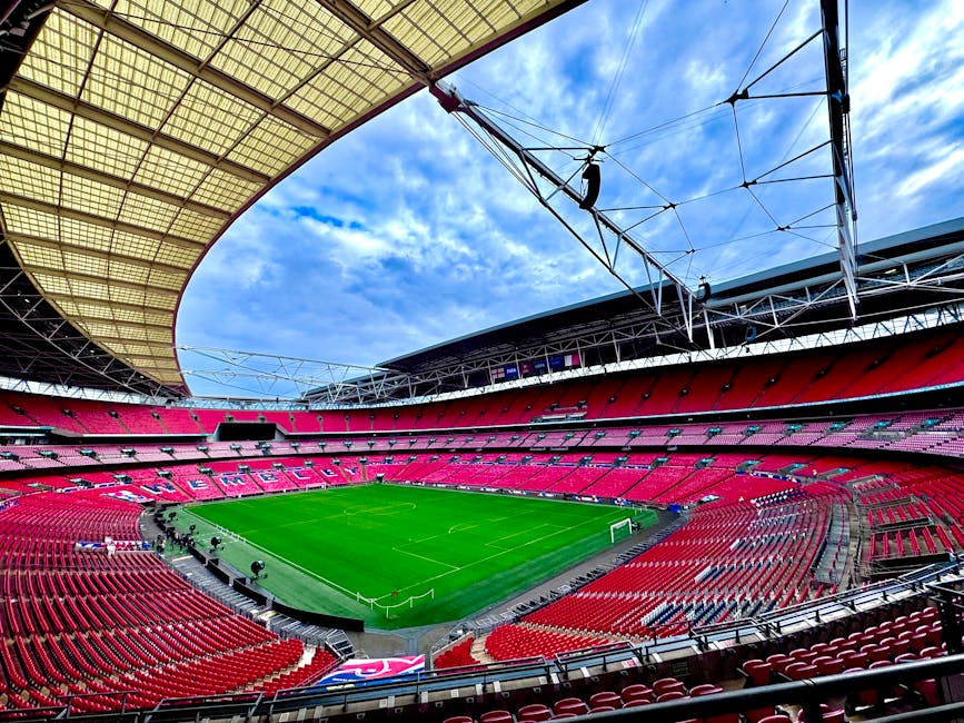 Interior view of Wembley Stadium showing a well-maintained grass football pitch with clearly marked white boundary lines and goalposts at each end. Surrounding the pitch are rows of red stadium seats 